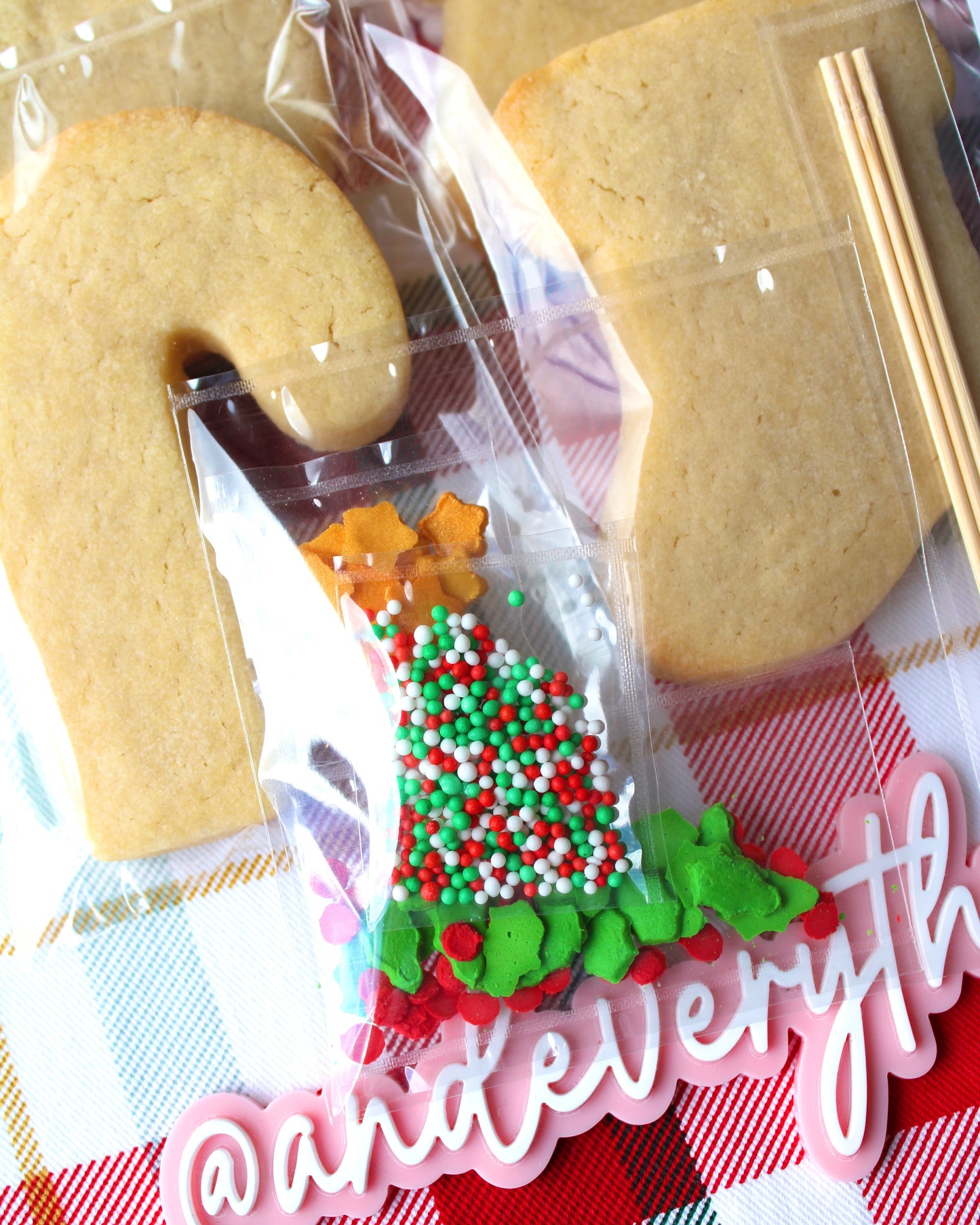 Close-up of a sprinkles packet filled with red, green, and white Christmas-themed sprinkles, featuring green holly leaves, red berry sprinkles, and gold star accents.