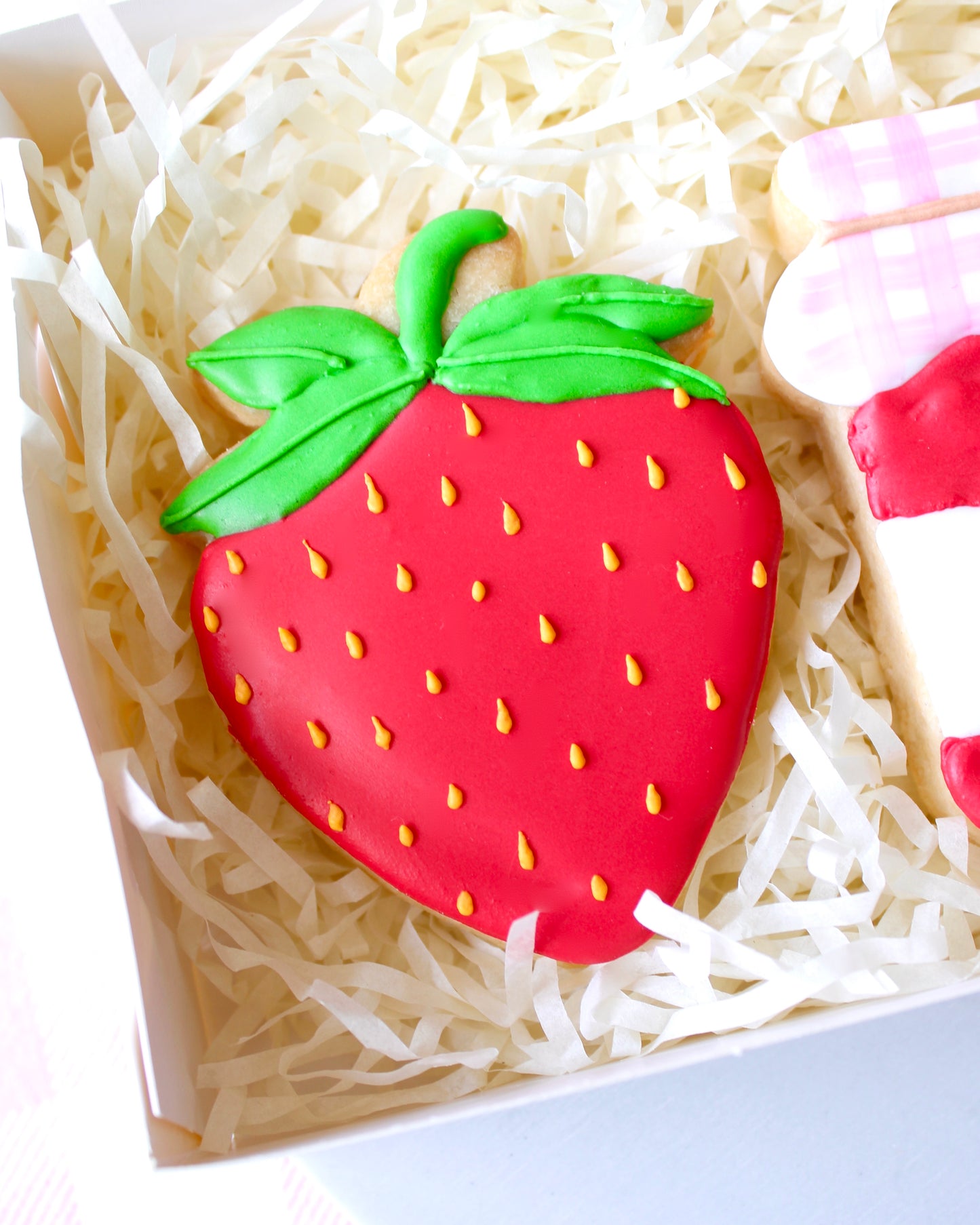 Close-up of a red strawberry cookie with yellow seeds and green leaves icing details.