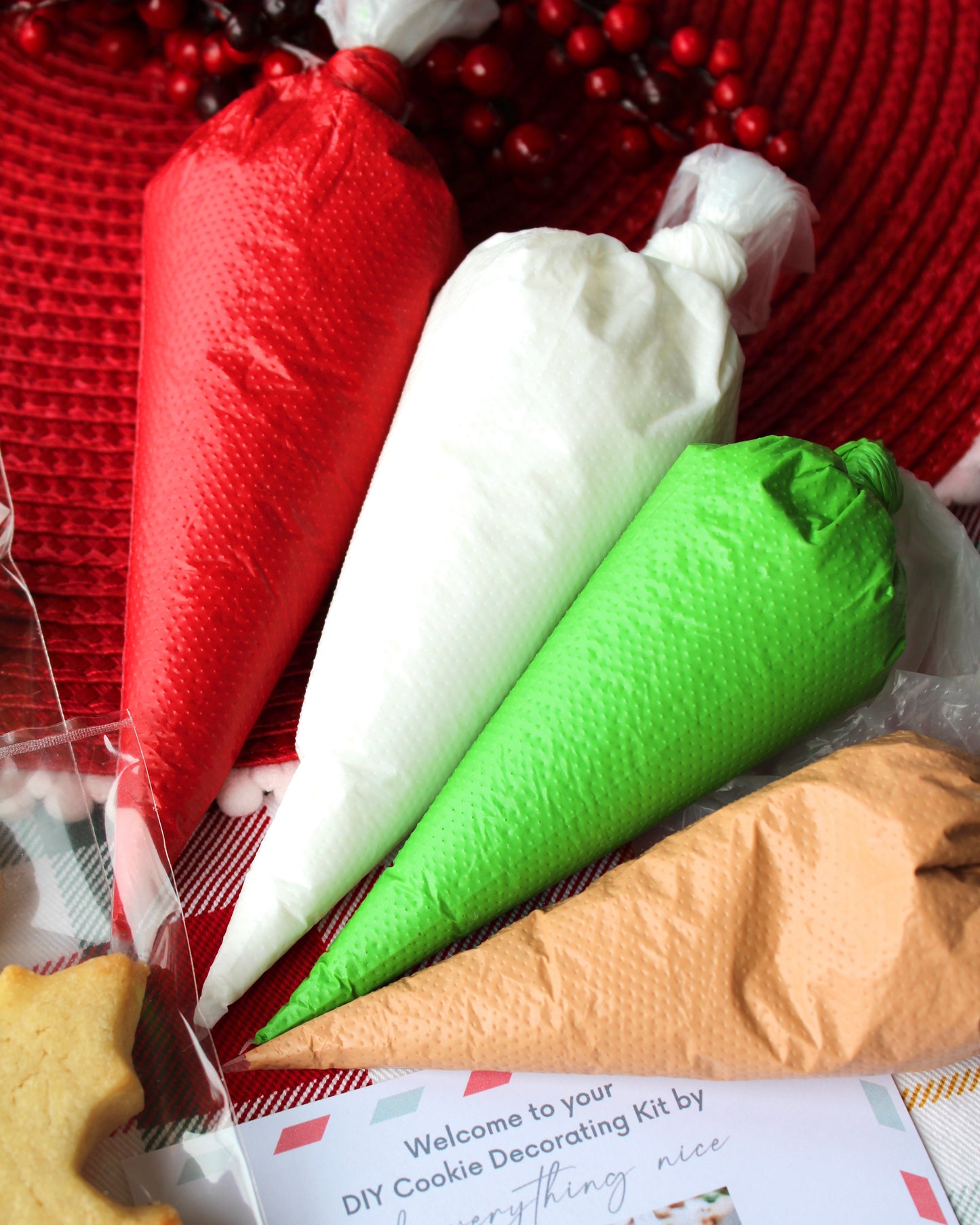 Close-up of four icing bags in red, green, white, and tan, styled on a red Christmas-themed background.