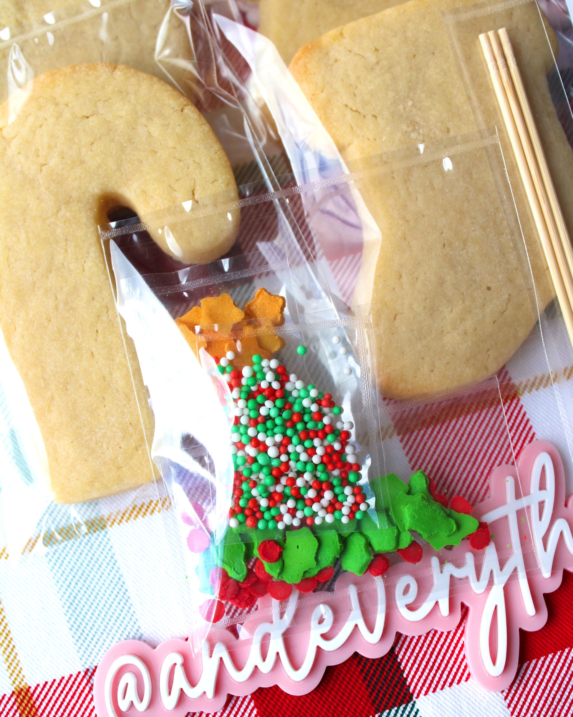 Close-up of a sprinkles packet filled with red, green, and white Christmas-themed sprinkles, featuring green holly leaves, red berry sprinkles, and gold star accents.
