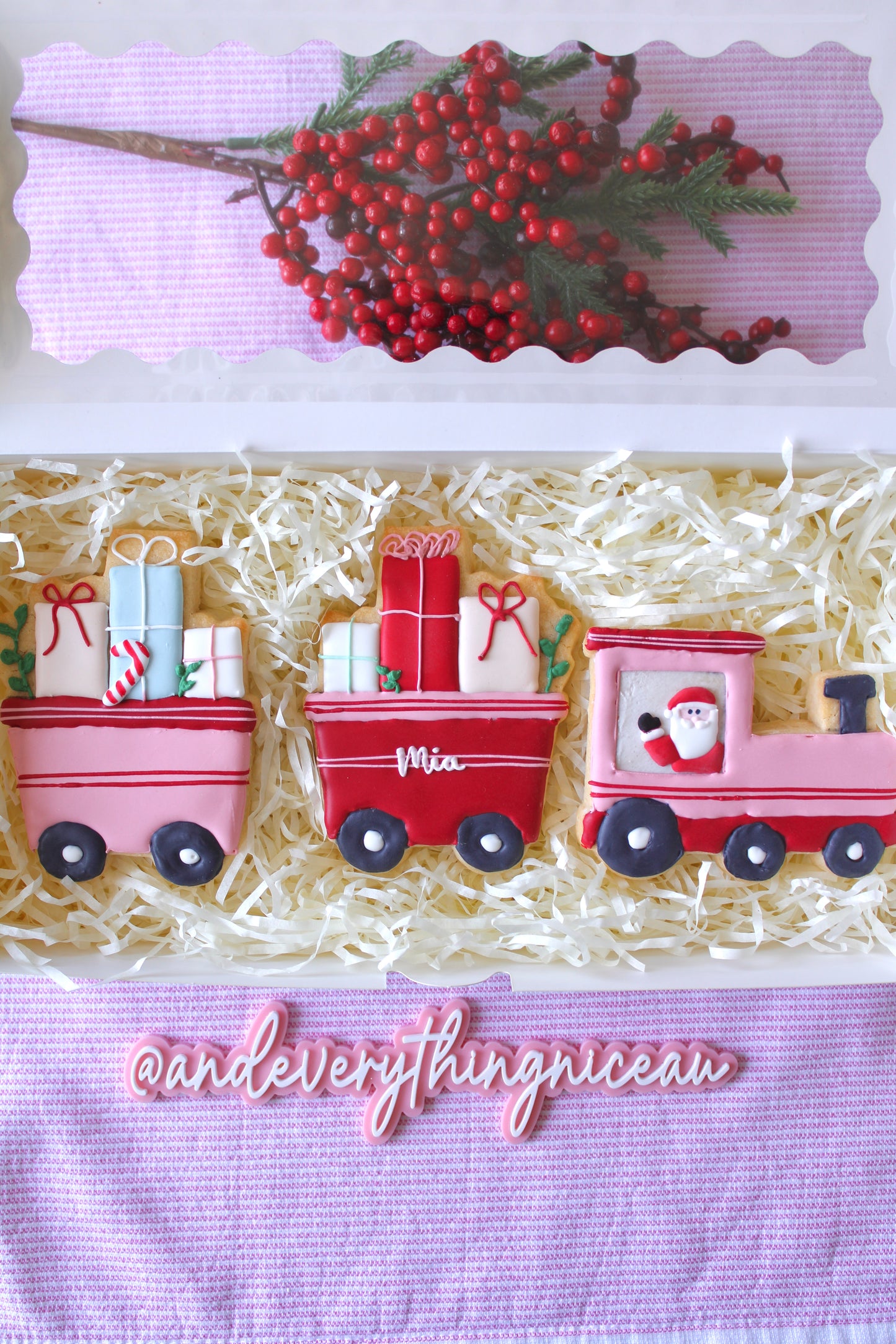 Christmas train-themed three-part pink and red cookie in a white gift box with clear window, styled on pink and white striped fabric, hand-decorated, perfect holiday gift.