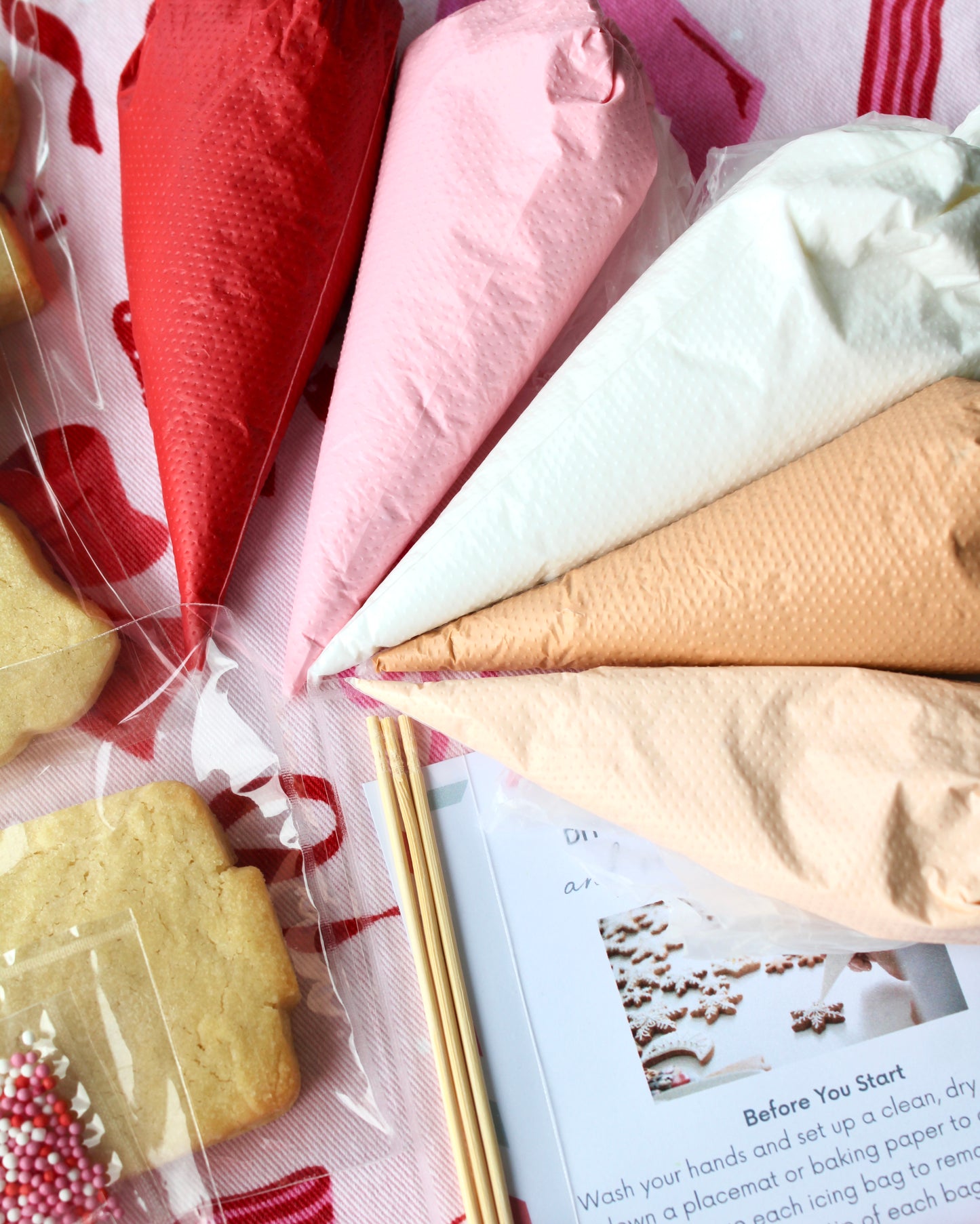 Close-up shot of five royal icing piping bags filled with red, pink, white, tan, and cream icing.