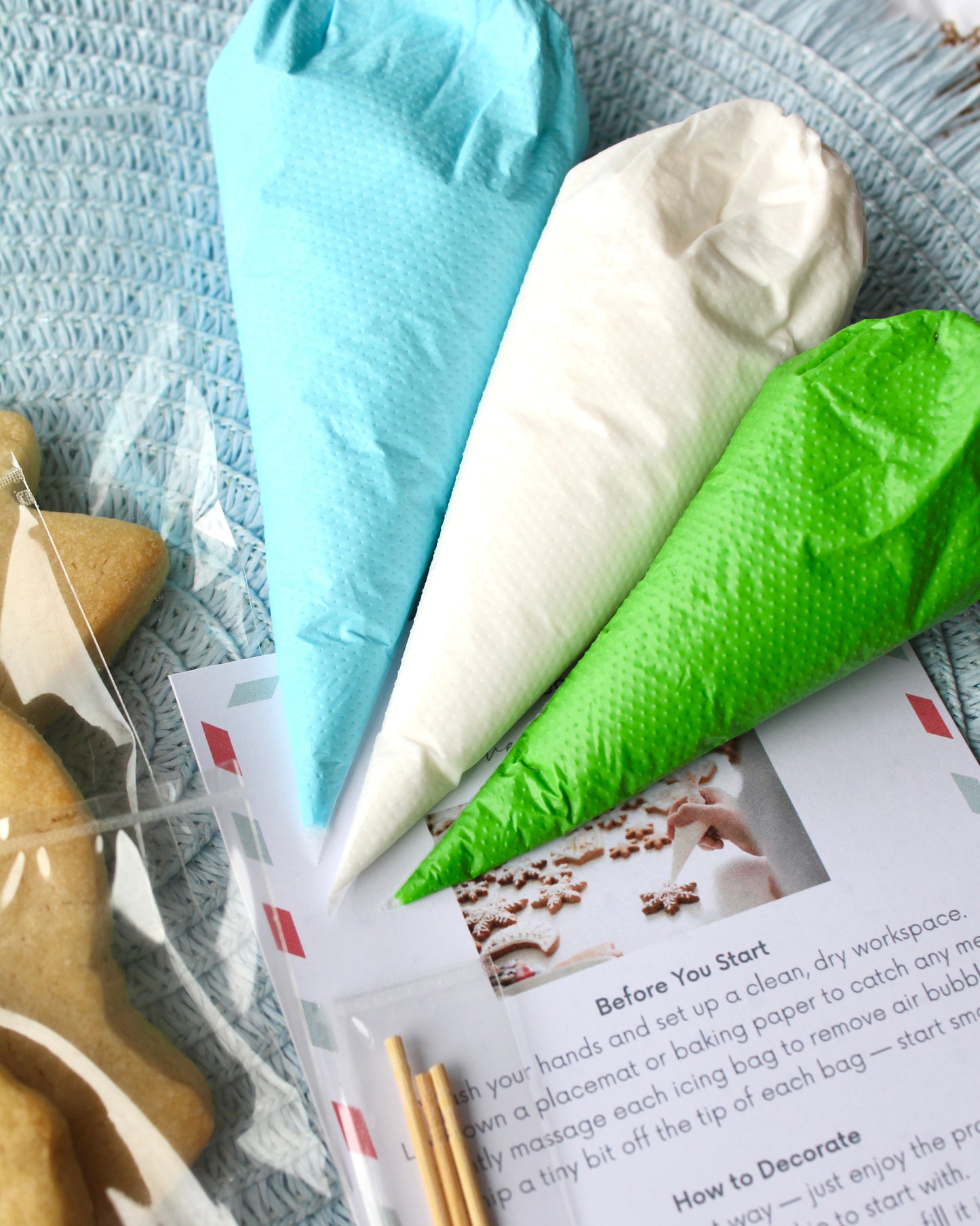 Close-up of blue, green, and white icing bags resting on top of an instruction card, placed on a pale blue placemat.