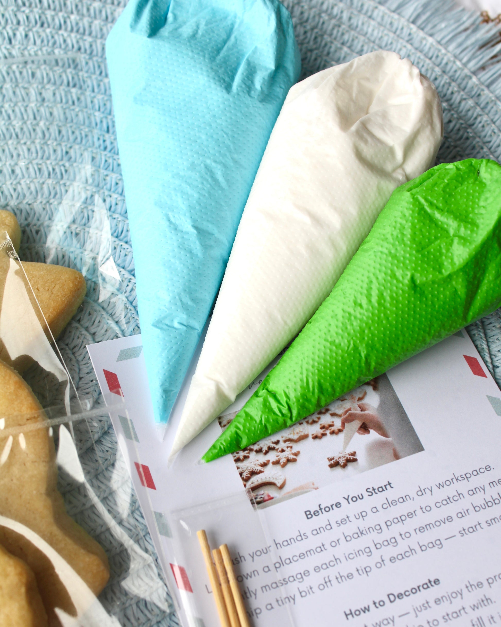 Close-up of blue, green, and white icing bags resting on top of an instruction card, placed on a pale blue placemat.