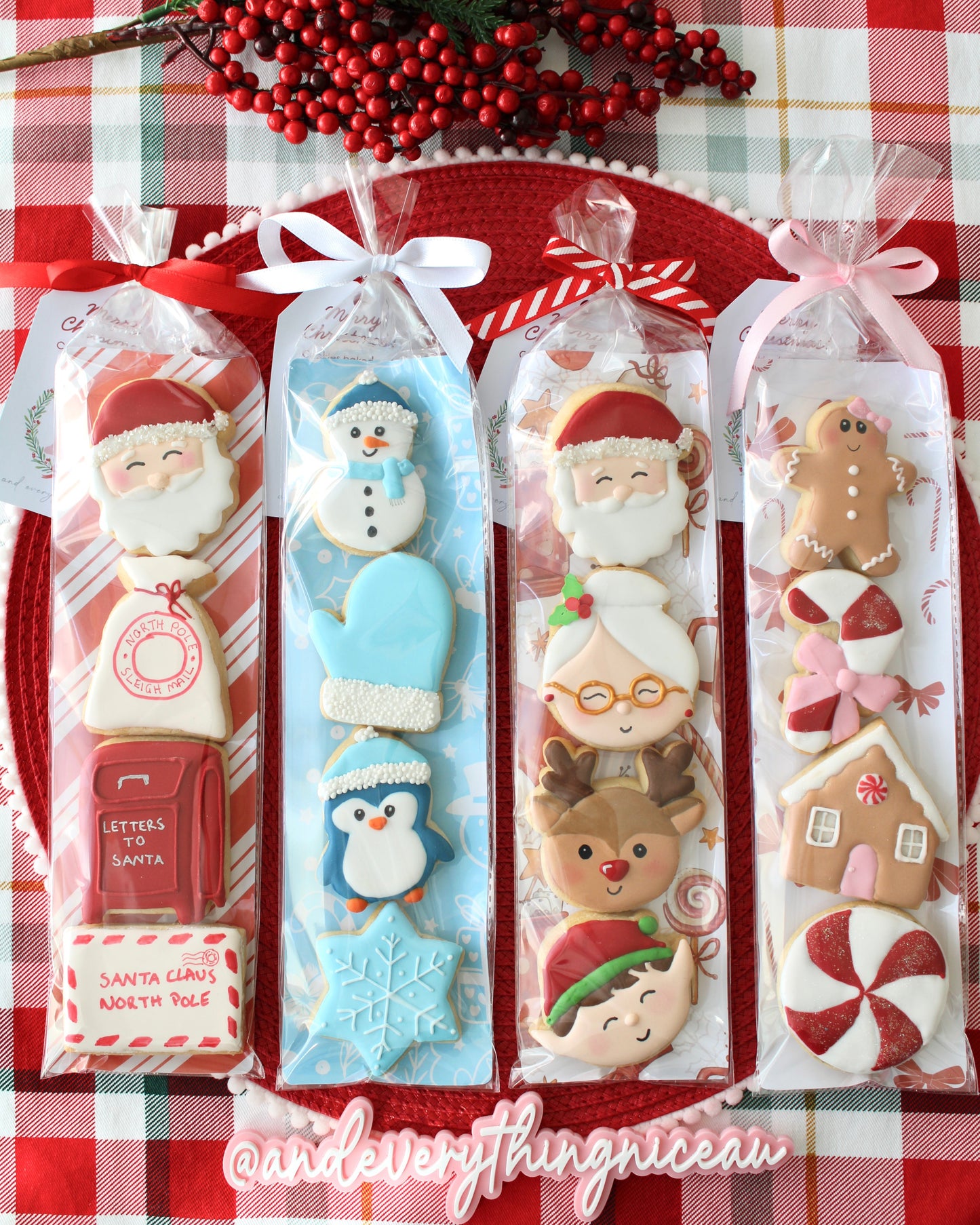 Four Christmas cookie packs, each in a different holiday-themed sleeve, tied with ribbons, styled on red and green tartan fabric