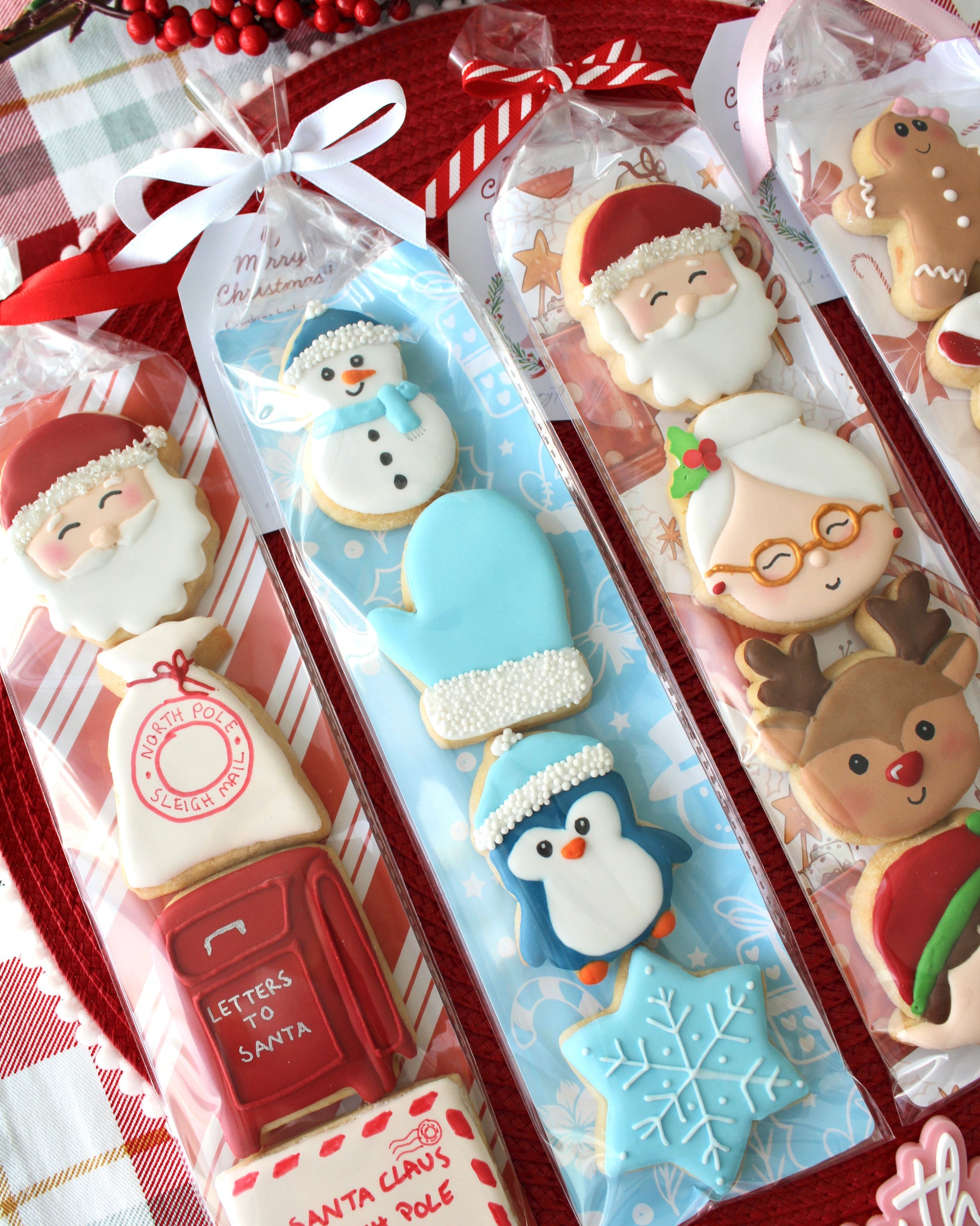 Close-up of a winter-themed cookie pack, including a snowman with pale blue beanie, pale blue mitten with white pearl cuff, dark blue penguin with pale blue beanie, and pale blue snowflake cookie, tied with a white bow