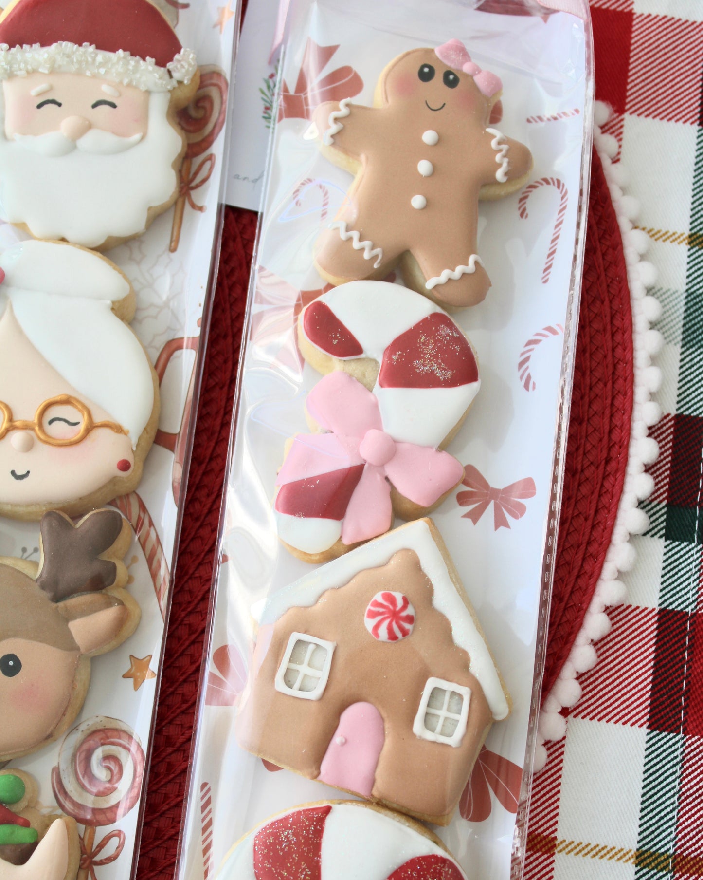 Close-up of a Christmas cookie pack, including a gingerbread girl with bow, red and white candy cane with pink bow, gingerbread house with pink door, and red and white peppermint swirl cookie, tied with a pink bow