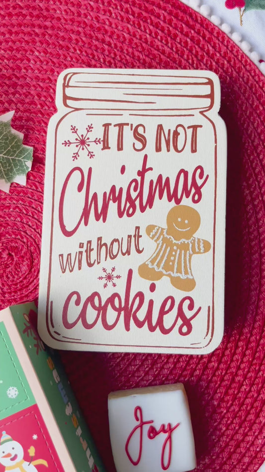 12 Days of Christmas cookie box featuring 12 mini Christmas-themed cookies arranged around the box, with a red cookie on top reading “Merry Christmas” in white cursive lettering. The cookies are decorated in festive red, green, white, and gold colours.
